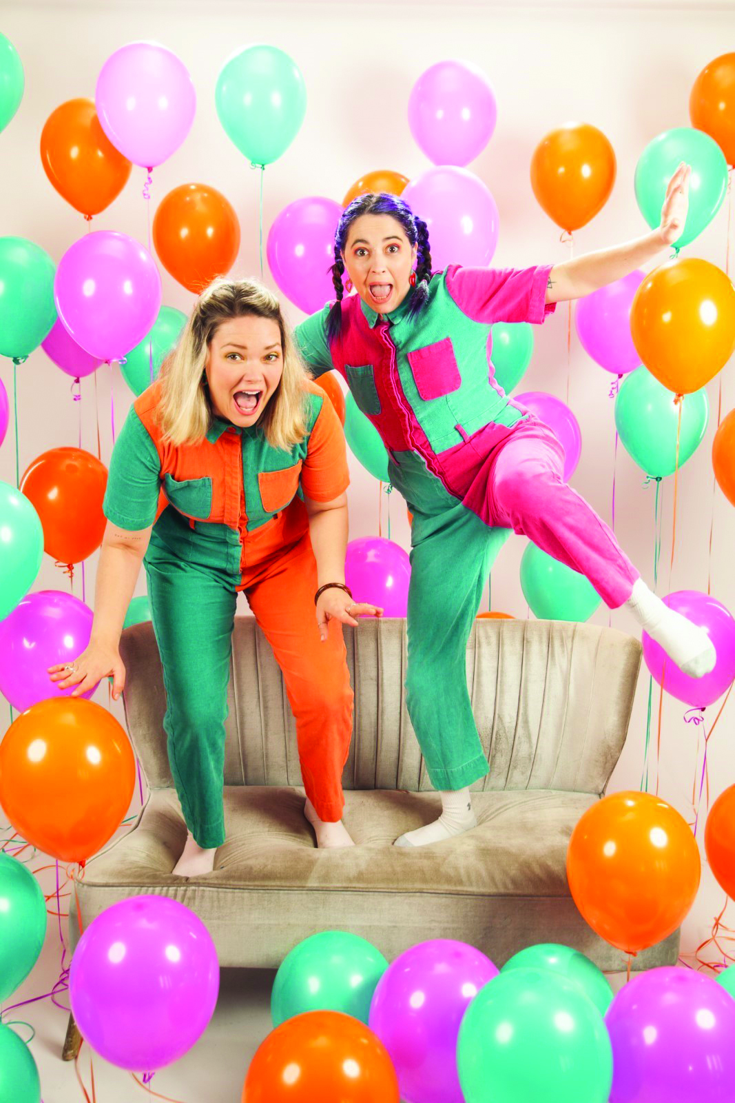 Two women standing on couch with dozens of floating baloons