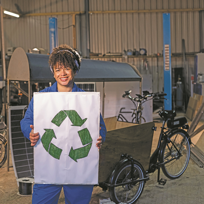 Woman standing in a bike repair workshop holding a recycling sign