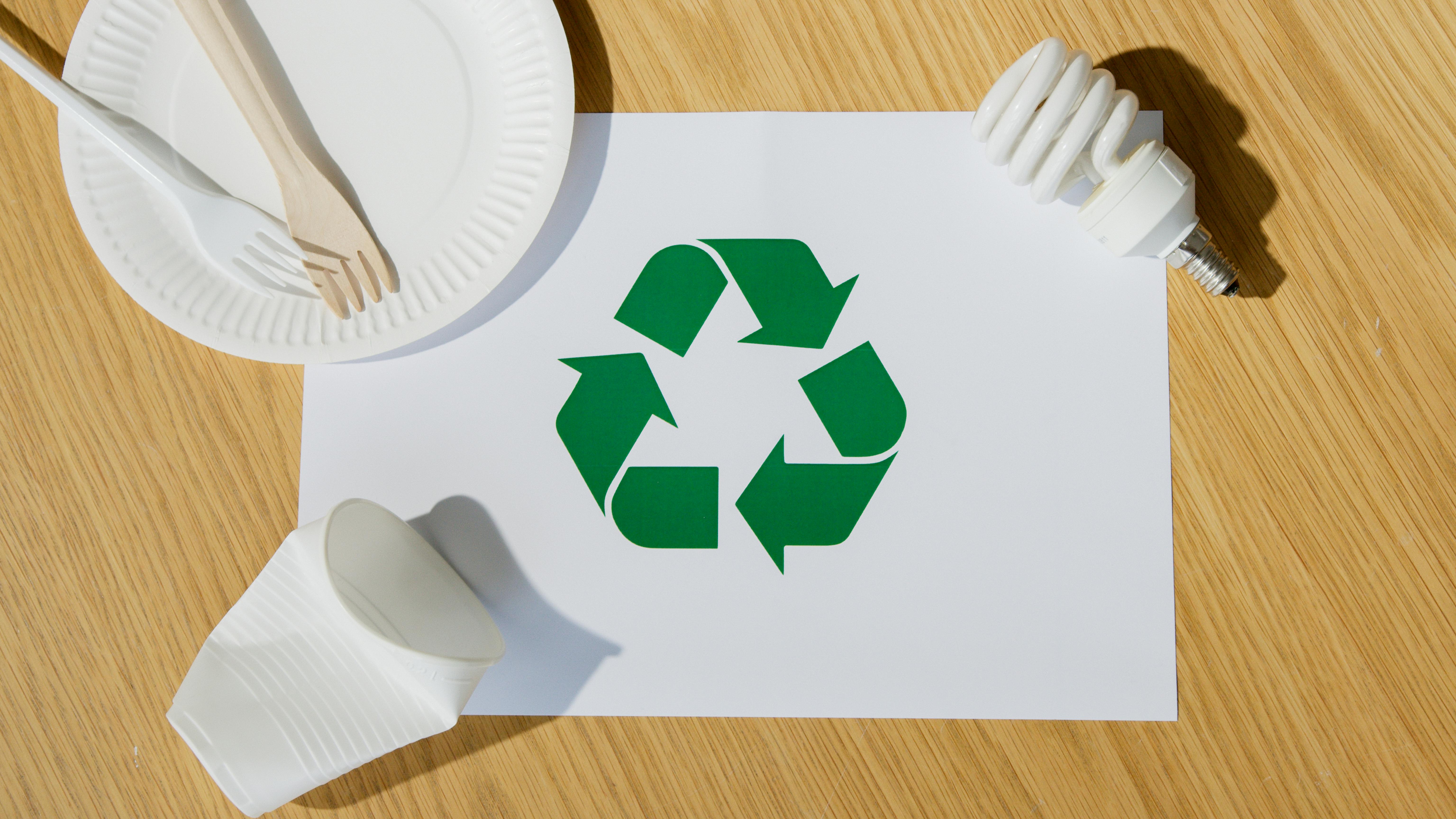 Green recycle symbol surrounded by paper plates and cups